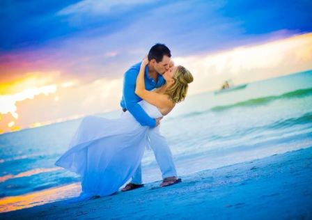 Image of a groom dipping his bride dance-style, the two of them kissing with a St. Pete beach as the background.