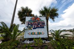 The sign for Pensacola Beach, white wood with a tropical font and palm trees in the background.
